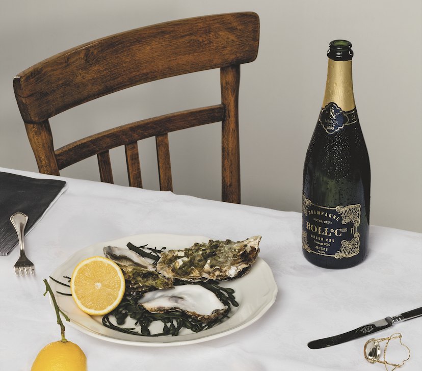 Grand Cru Vintage bottle beside a plate of oysters and lemon on a white tablecloth